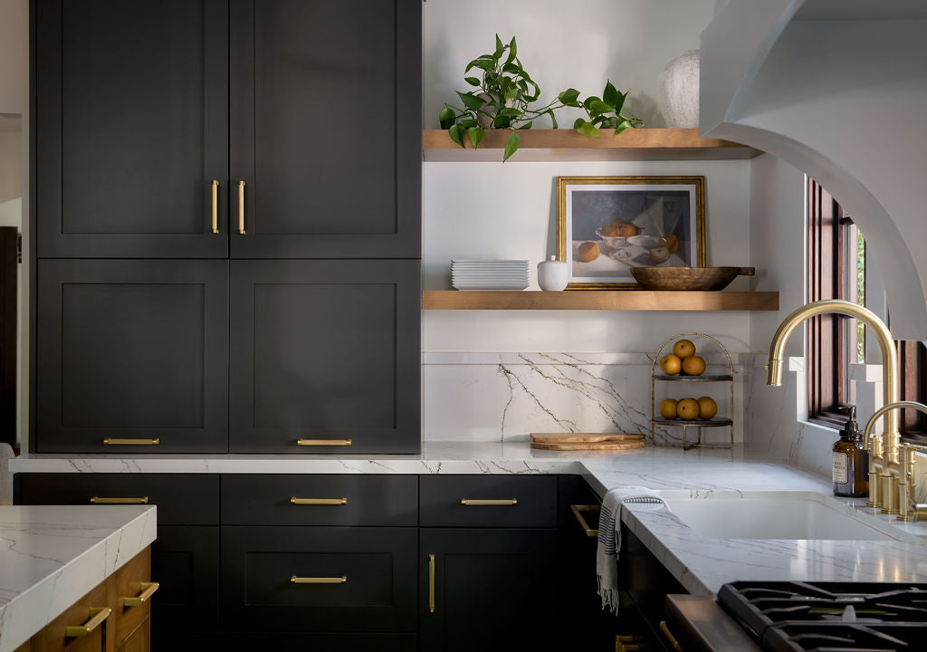 Modern kitchen with black cabinets, white countertops, and gold fixtures.